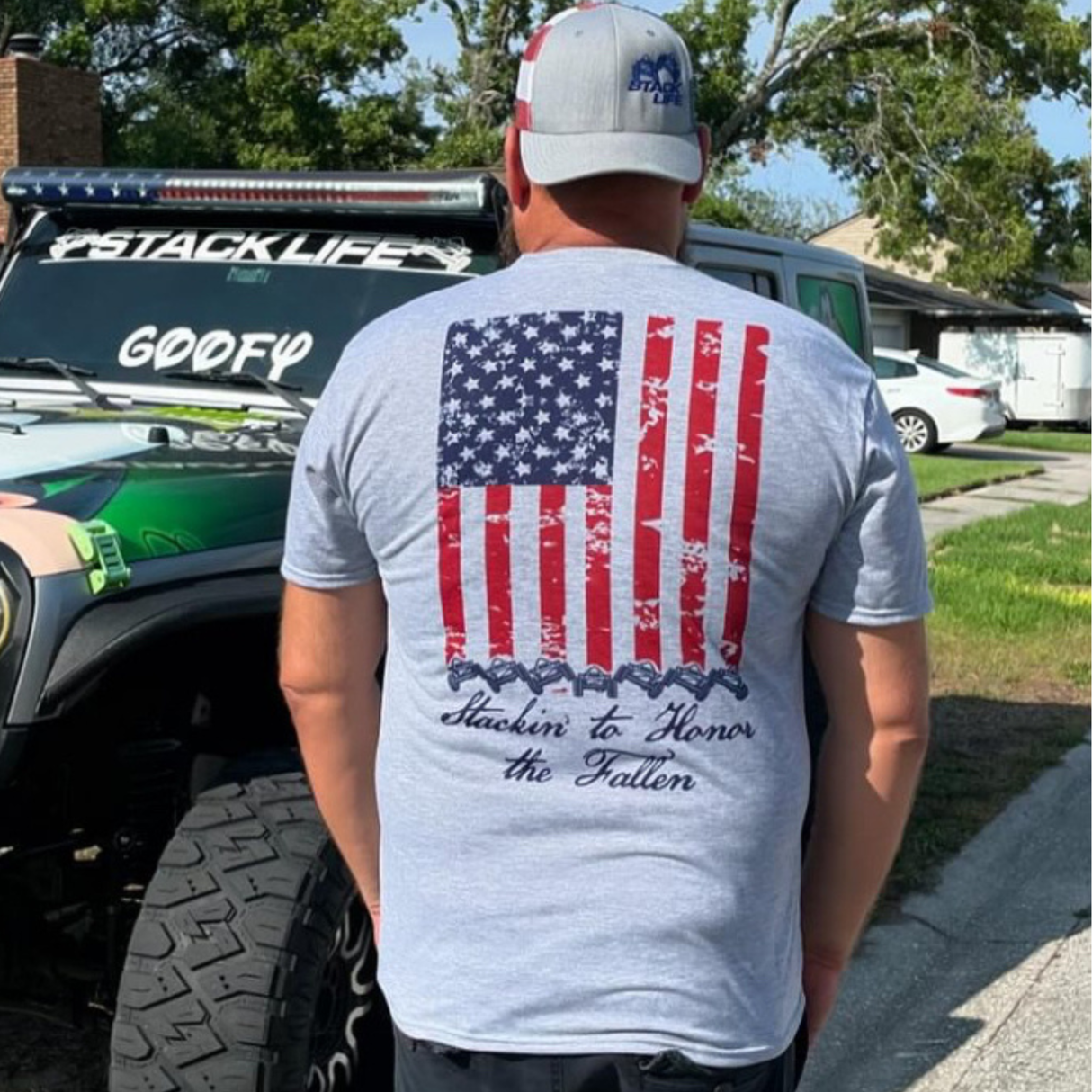 Person wearing a gray t-shirt with an American flag design and text that stays stackin to honor the fallen
, standing in front of a truck.