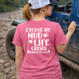 Person wearing a pink t-shirt with text Excuse my mudlife crisis standing next to a muddy jeep