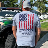 Person wearing a gray t-shirt with an American flag design and text that stays stackin to honor the fallen
, standing in front of a truck.