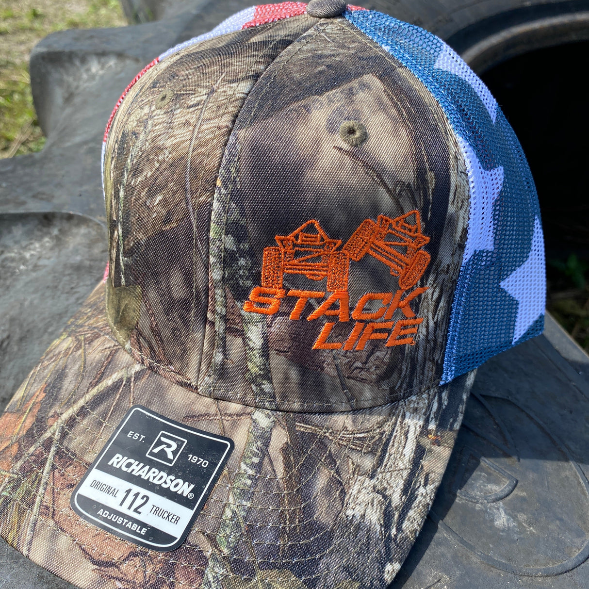 american flag camo hat with orange stack life logo