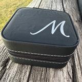 Side view of black leatherette jewelry box with silver M in script engraved on the top