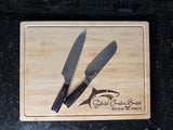 Wooden cutting board with two knives on a black surface, featuring a shark logo and text.