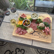 Wooden charcuterie board with meats, cheeses, and olives on a patio table with glasses of wine.