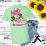 Light green t-shirt with pink text, jeans, and sneakers on a wooden surface with sunflowers. Mud And Mascara logo in pink
