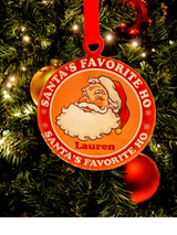 
Vintage-style acrylic Christmas ornament featuring a winking Santa, the text "Santa's Favorite Ho," and a customizable name in festive colors, hanging on a tree.